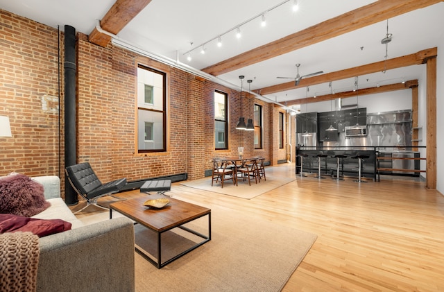 living room with brick wall, wood finished floors, a ceiling fan, beamed ceiling, and a wood stove