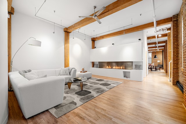 living room with a glass covered fireplace, brick wall, ceiling fan, wood finished floors, and beam ceiling