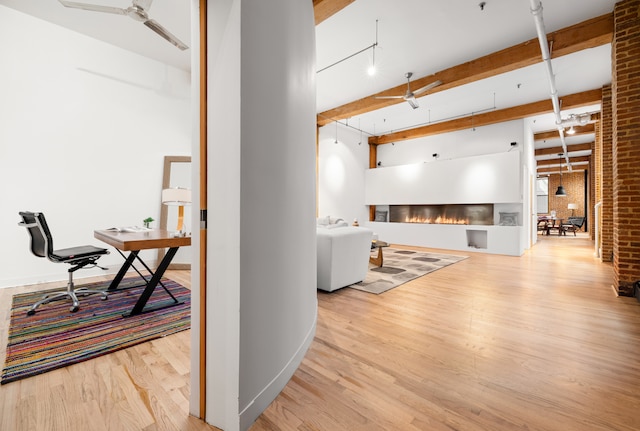 interior space with a ceiling fan, a glass covered fireplace, brick wall, wood finished floors, and beamed ceiling