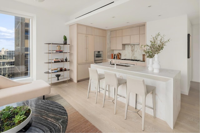 kitchen featuring light brown cabinets, a sink, a kitchen breakfast bar, tasteful backsplash, and light wood-style floors