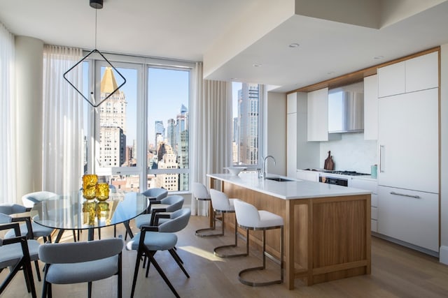 kitchen featuring plenty of natural light, hanging light fixtures, an island with sink, white cabinets, and sink