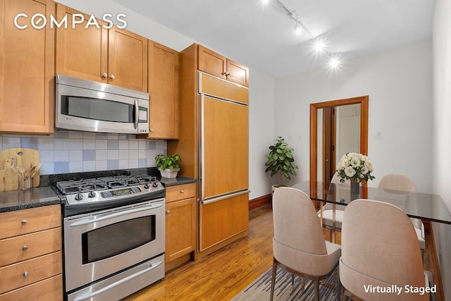 kitchen with stainless steel appliances, dark stone countertops, light hardwood / wood-style flooring, and decorative backsplash