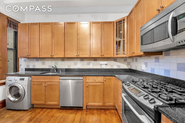 kitchen featuring washer / clothes dryer, appliances with stainless steel finishes, sink, and dark stone counters