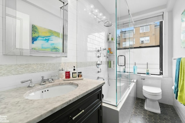 full bathroom with shower / bath combination with glass door, tile walls, vanity, tile patterned floors, and toilet