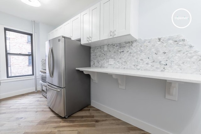 kitchen featuring white cabinets, a breakfast bar, freestanding refrigerator, light countertops, and light wood-style floors