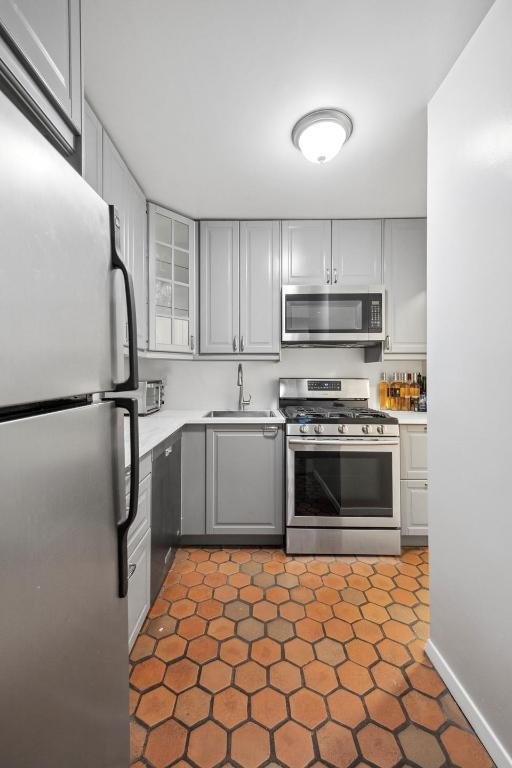 kitchen with stainless steel appliances, dark tile patterned floors, sink, and gray cabinetry