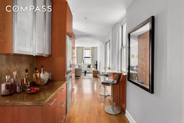 corridor with baseboards, arched walkways, and light wood-type flooring