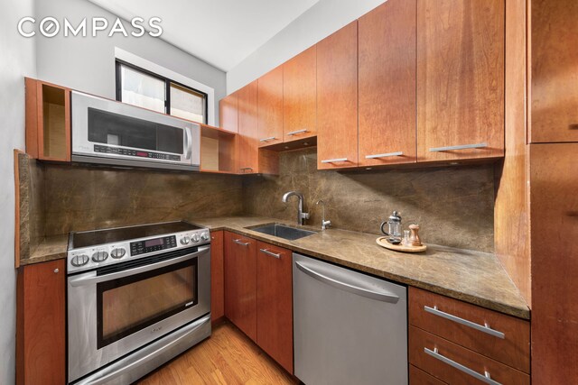 kitchen with backsplash, light wood-type flooring, appliances with stainless steel finishes, brown cabinetry, and a sink