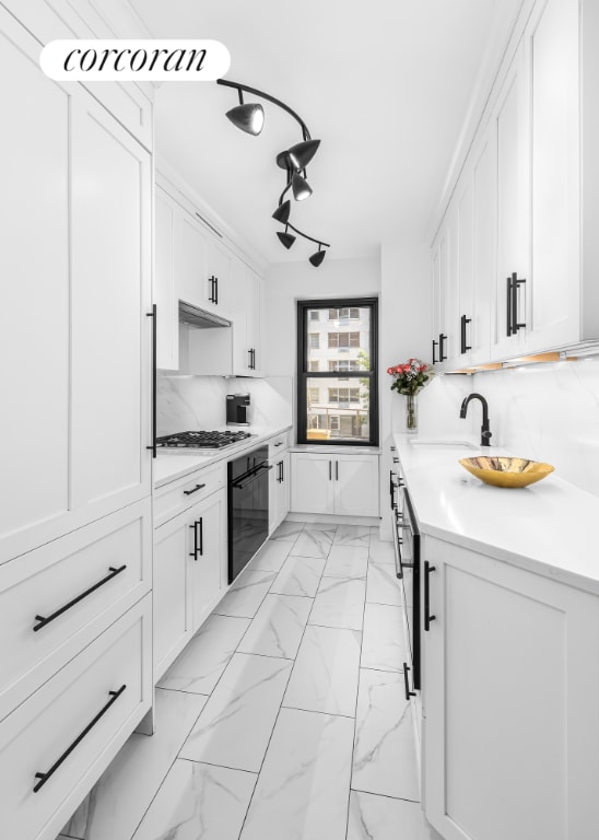 kitchen with decorative backsplash, black oven, white cabinetry, and sink