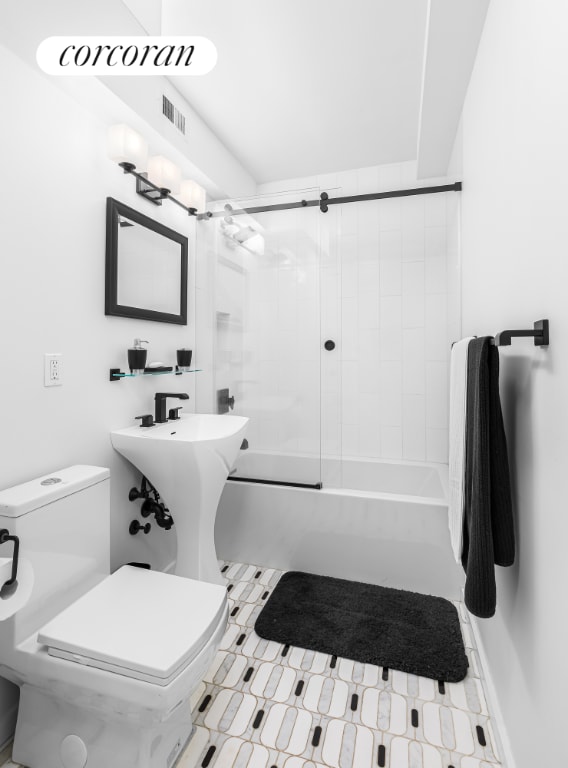 bathroom featuring toilet and shower / bath combination with glass door