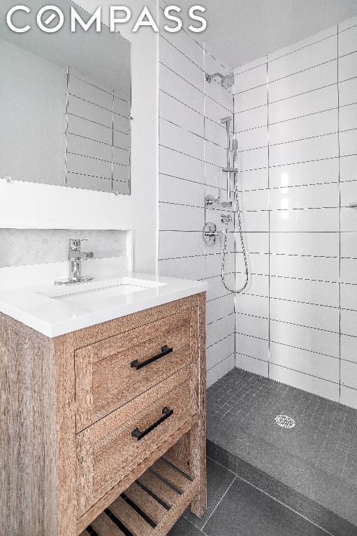 bathroom featuring tile patterned flooring, a tile shower, and vanity