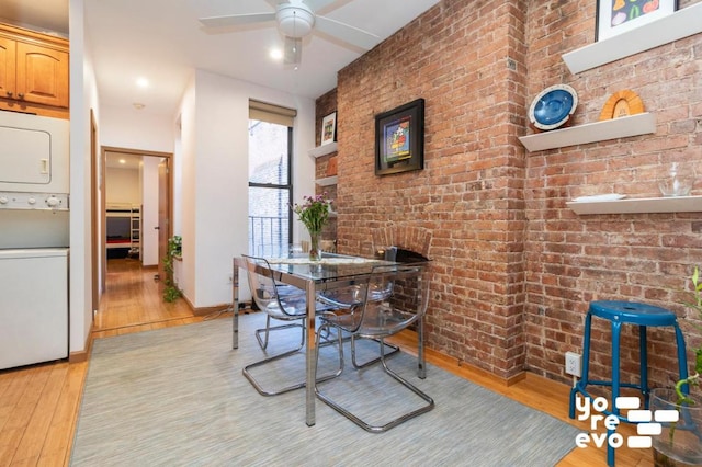 dining area featuring light wood-type flooring, ceiling fan, brick wall, and stacked washer and clothes dryer