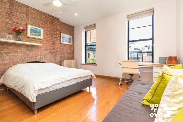 bedroom with ceiling fan, brick wall, radiator heating unit, and hardwood / wood-style floors