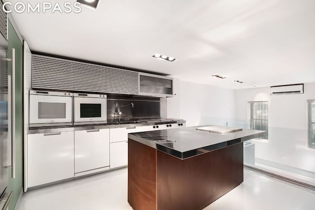 kitchen featuring white cabinetry, a wall mounted AC, a center island, oven, and sink