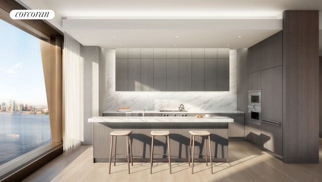 kitchen featuring tasteful backsplash, a center island, a kitchen bar, light hardwood / wood-style flooring, and a water view