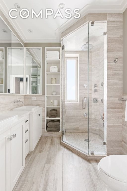 bathroom with tile walls, vanity, walk in shower, toilet, and crown molding