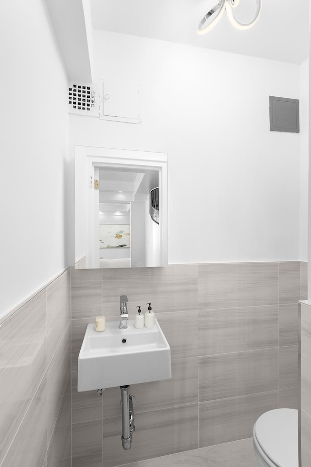 half bath featuring a wainscoted wall, a sink, tile walls, and toilet