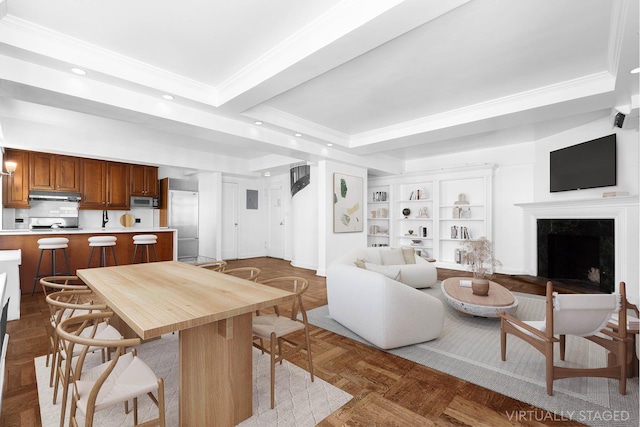 kitchen with under cabinet range hood, light countertops, appliances with stainless steel finishes, a raised ceiling, and crown molding