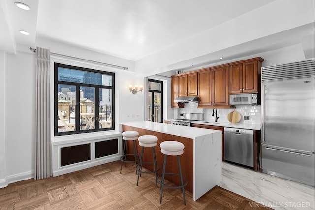 kitchen with a breakfast bar area, stainless steel appliances, tasteful backsplash, light countertops, and under cabinet range hood