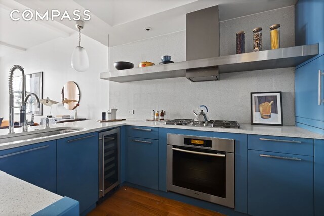 kitchen featuring wall chimney range hood, sink, stainless steel appliances, wine cooler, and blue cabinets