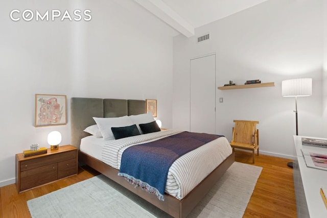 bedroom with beamed ceiling, wood finished floors, visible vents, and baseboards