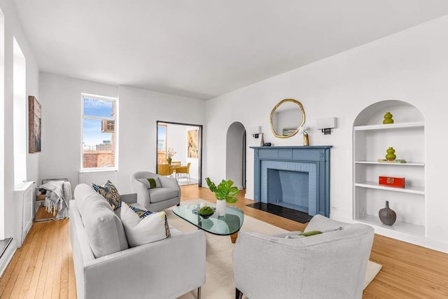 living room featuring arched walkways, light wood finished floors, a fireplace, and built in features