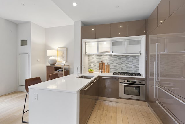 75 Wall St Unit 34M, New York City, NY 10005 - kitchen with appliances with stainless steel finishes, modern cabinets, a peninsula, a sink, and light wood-style flooring