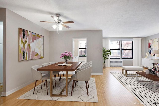 dining area with a textured ceiling, light wood-style flooring, a ceiling fan, baseboards, and radiator heating unit