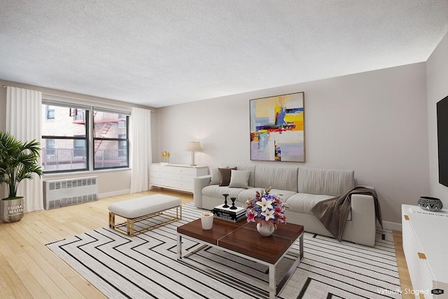 living room with light wood-style floors, radiator, a textured ceiling, and baseboards