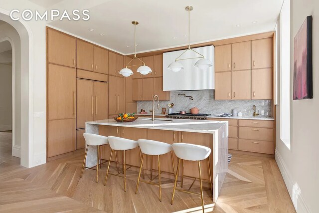 kitchen with light countertops, decorative backsplash, a kitchen breakfast bar, arched walkways, and a sink