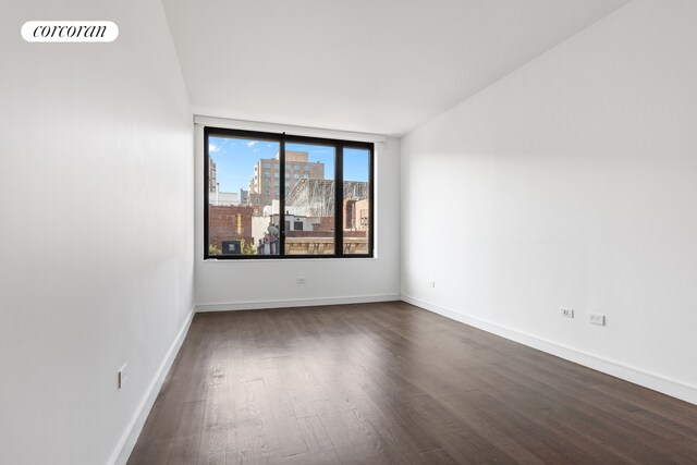 spare room featuring dark wood-style floors, visible vents, baseboards, and a city view