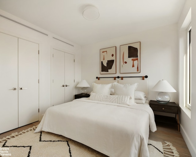 bedroom with wood finished floors, baseboards, and two closets