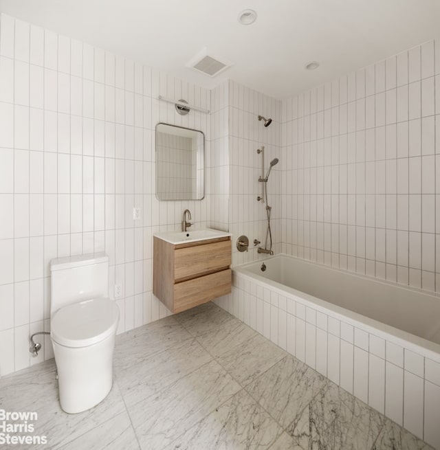 bathroom with vanity, tiled shower / bath, toilet, and tile walls