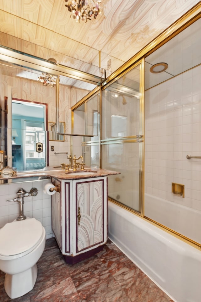 bathroom featuring toilet, bath / shower combo with glass door, tile walls, and vanity