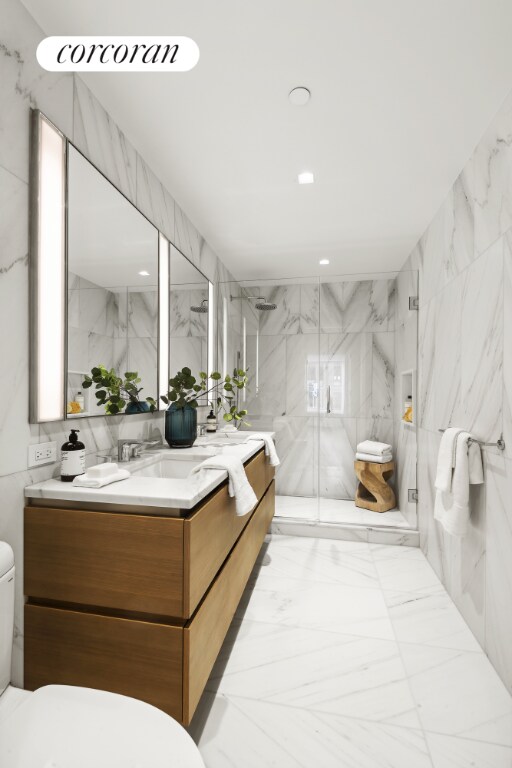 bathroom with a shower with door, vanity, tile walls, and toilet