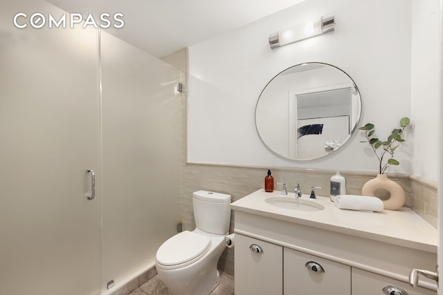 bathroom with toilet, a shower stall, vanity, and tile walls