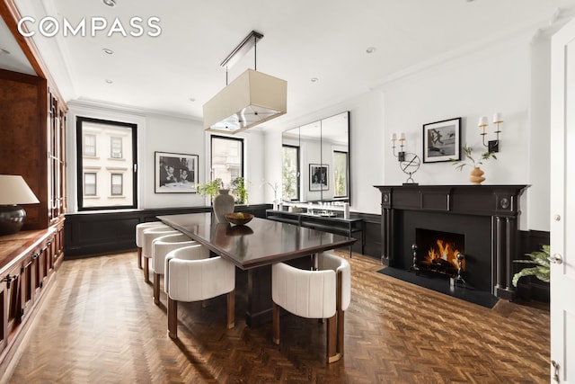 dining area with a fireplace with flush hearth, wainscoting, and crown molding