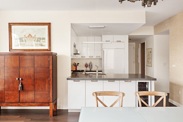 kitchen with paneled fridge, a breakfast bar, a peninsula, white cabinetry, and dark countertops