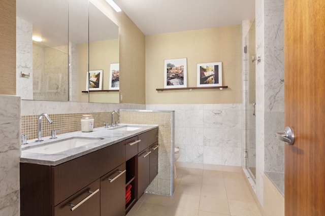 bathroom featuring toilet, double vanity, a sink, and tile walls