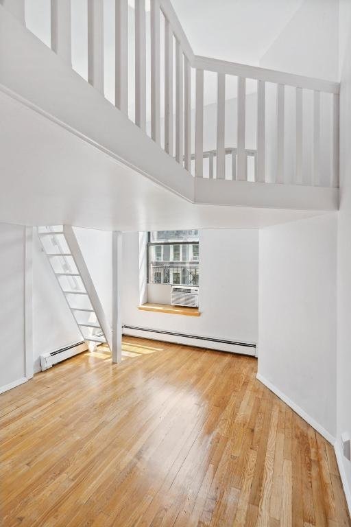 unfurnished living room featuring a baseboard heating unit, baseboards, a high ceiling, and wood finished floors