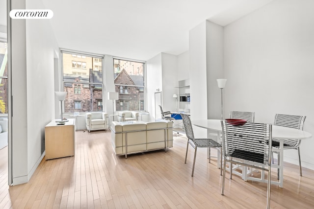 dining room with light wood-type flooring, a healthy amount of sunlight, and a wall of windows