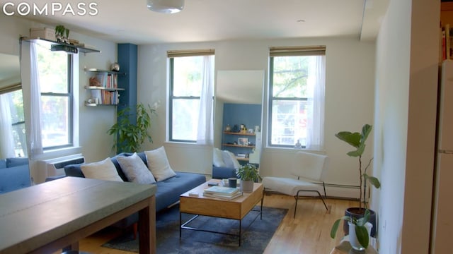 sitting room with a baseboard heating unit, hardwood / wood-style flooring, radiator heating unit, and a healthy amount of sunlight