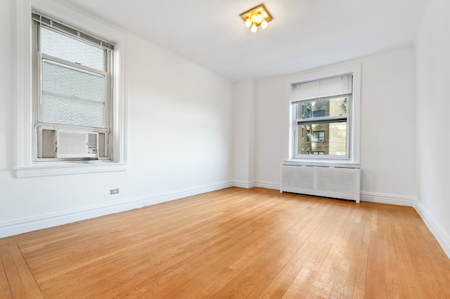 unfurnished room featuring light wood finished floors, radiator heating unit, and baseboards