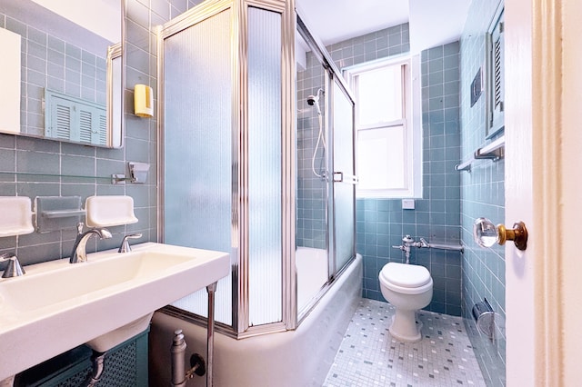 bathroom with tile walls, toilet, enclosed tub / shower combo, tile patterned flooring, and a sink