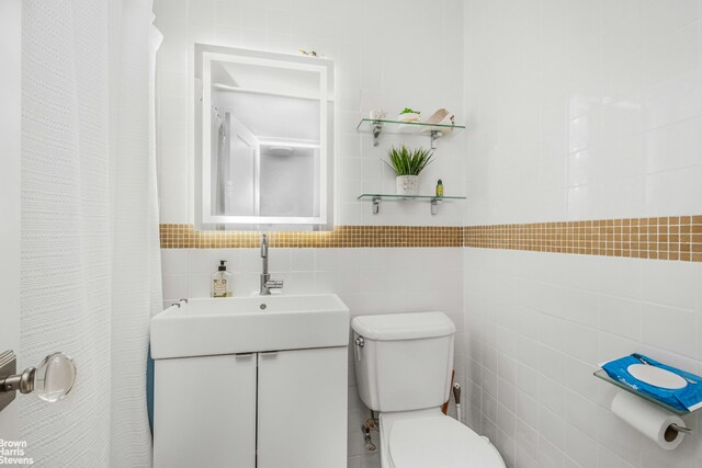 bathroom with tile walls, toilet, and vanity