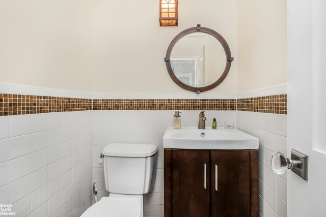 half bath featuring toilet, a wainscoted wall, tile walls, and vanity