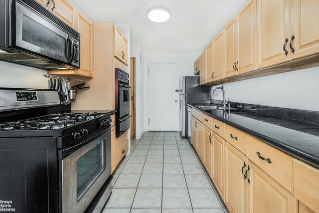 kitchen with light brown cabinetry, appliances with stainless steel finishes, dark countertops, and a sink