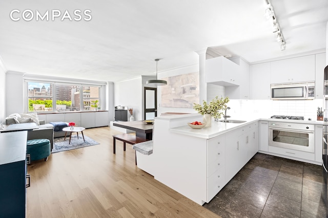 kitchen with appliances with stainless steel finishes, open floor plan, light countertops, ornamental molding, and a sink