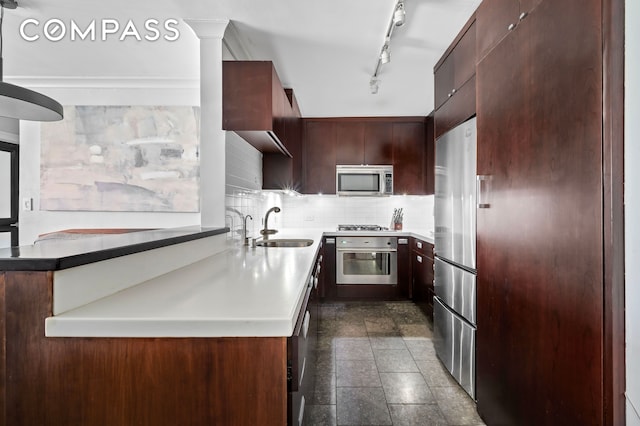 kitchen featuring appliances with stainless steel finishes, a sink, decorative backsplash, rail lighting, and a peninsula