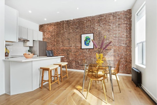 kitchen with kitchen peninsula, stainless steel fridge, a breakfast bar area, radiator, and white cabinets